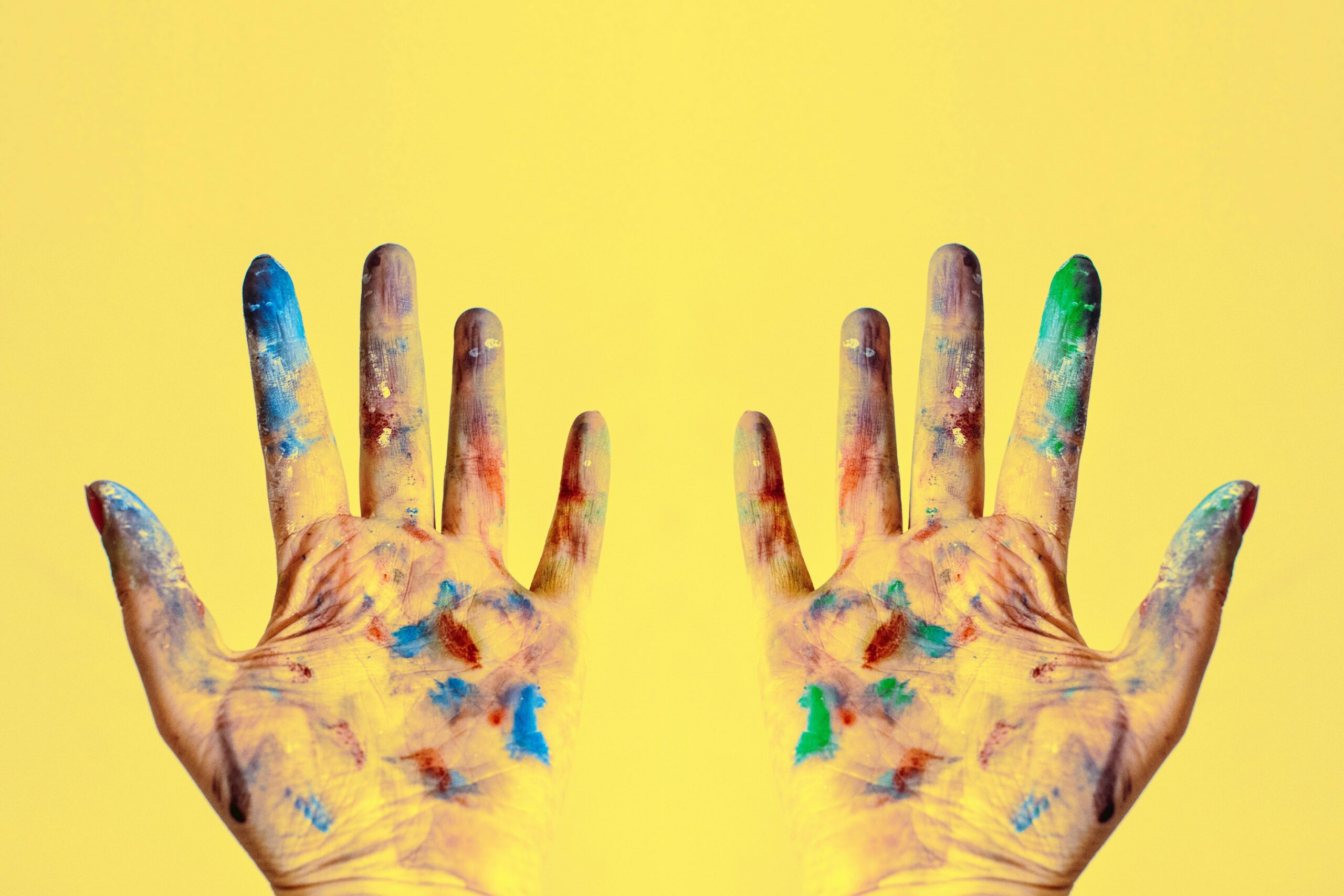 Colorful fingers spread against a bright yellow backdrop, showcasing creativity.