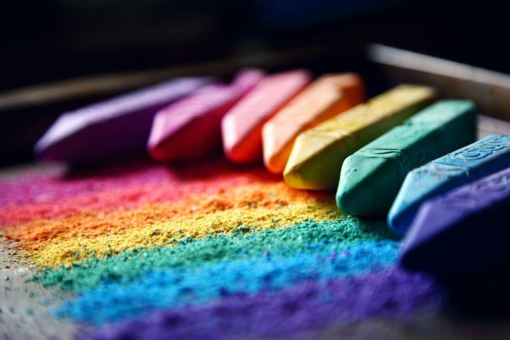 Close-up of vibrant colored chalks forming a rainbow pattern against a dark background.