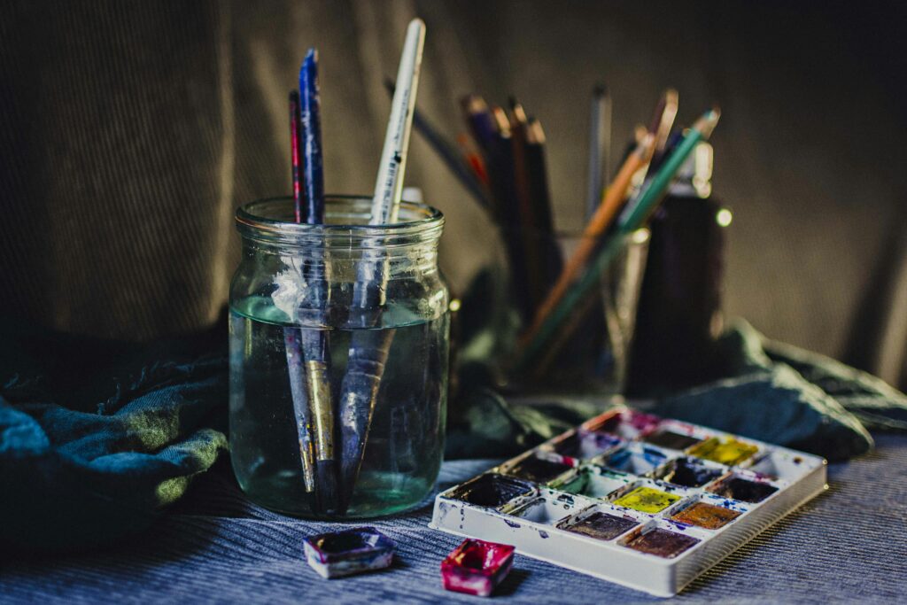 A creative still life of paintbrushes in a jar with watercolors and pencils, perfect for artistic inspiration.