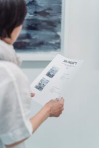 A woman examines an art project document at a gallery, focusing intently on the details.