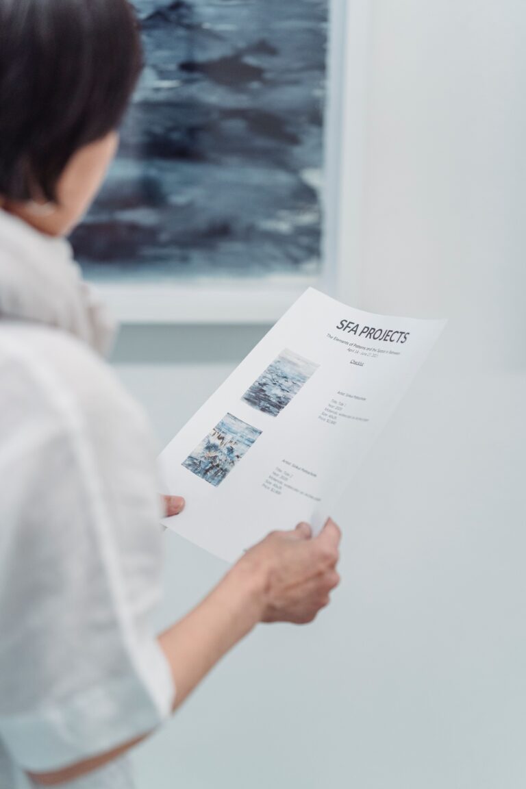 A woman examines an art project document at a gallery, focusing intently on the details.