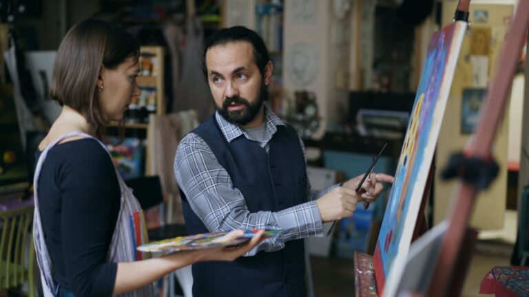Art teacher guiding a student in painting techniques at an indoor studio.